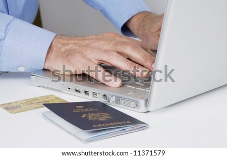 mature man typing on laptop computer with passport and credit card next to him