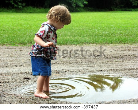 Curly haired little girl playing in a mud puddle