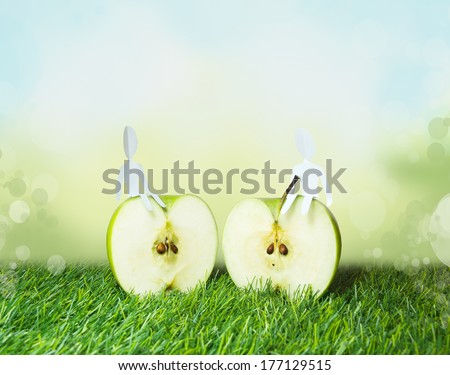 two Paper men sitting on ripe green apple