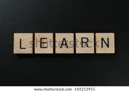 The word learn spelled out with wooden blocks on a black chalk board.