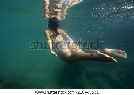 Beautiful girl in bikini swimming underwater in the ocean on a clear day.