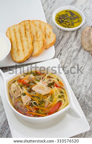 rustic chicken soup with noodles and vegetables close-up over wooden vintage background