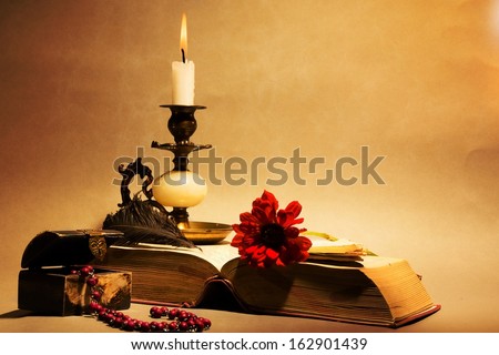 Still life. Candle, old book, feather, pen, small chest on orange background.
