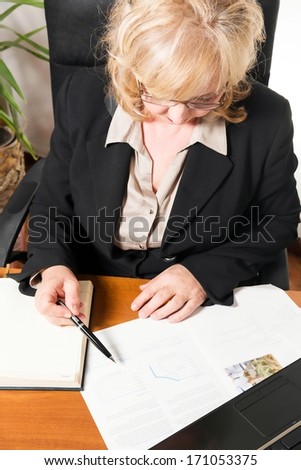 Middle aged businesswoman, writing document in the office.