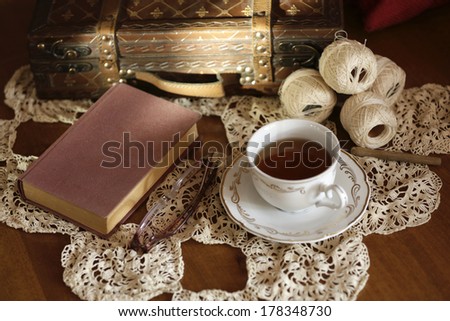 Cup of tea, book and glasses on old wooden table.