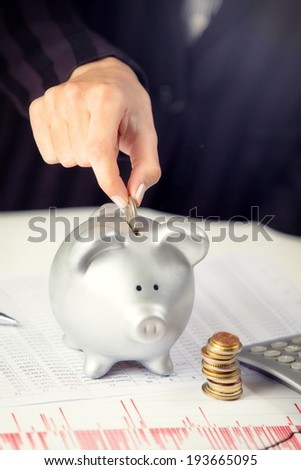 Female hand putting coin in piggy bank, on the office desk.