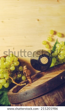 Bottle of wine, green grapes and old barrel, placed on wooden table, in light cellar- top view.