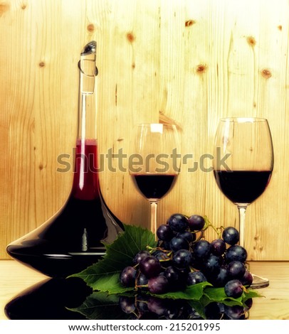 Luxury wine collection- two glasses, bottle, and dark blue grapes. Light wooden background and reflection table.