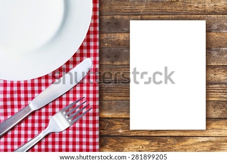 Menu concept. White plate, fork and knife placed on old wooden table with red checked tablecloth and empty place for text. Top view.