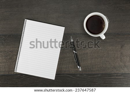 Blank page of a notepad and pen together with a cup of tea on dark wooden background.