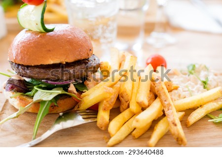 Hamburger with lettuce and french fries served on a wooden plate with a tight composition and short depth of field in a restaurant Environment.