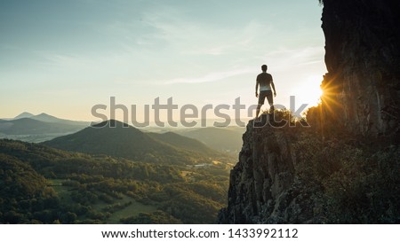 Travel man tourist alone on the edge cliff mountains and looking on the valley. Silhouette of the person on the high rock at sunset. Hiking adventure lifestyle extreme vacations.