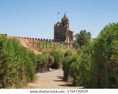 Ornate entrance, with bell tower, Porta da Vila known as Village Door or Porta Nova visible in the distance. Remains of ancient castle or Castelo de Montemor-o-Novo and stone masonry wall ruins. Foto stock © 