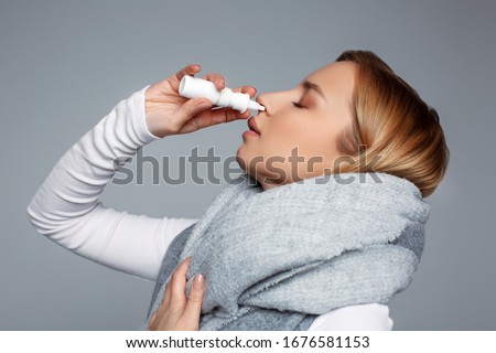 Female wrapped in scarf using nasal spray medicine for runny nose . Seasonal health issues. Allergic chronic rhinitis, common cold, sinusitis concept. First symptoms of flu, virus or disease Zdjęcia stock © 
