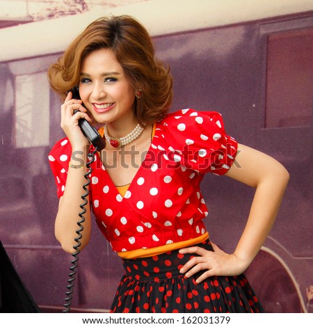 Charming pin-up woman with retro hairstyle and make-up talking on the phone.