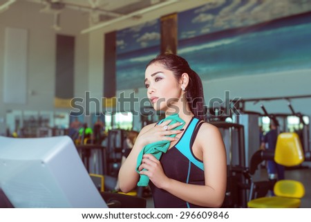 Attractive asian girl running on the treadmill in the gym with towel after training