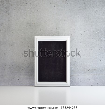 Black board in white frame on a white floor near concrete wall