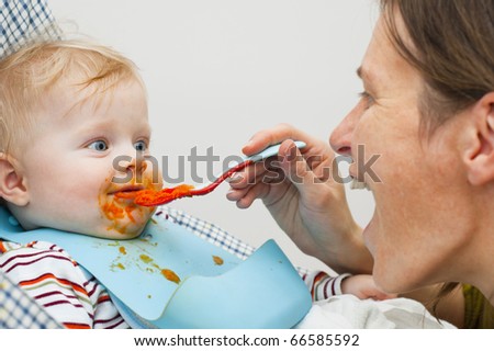 Little kid dirty on his face by the food and mother feeding him