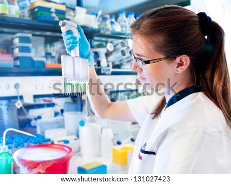 Young female tech or scientist works with multichannel pipette in biological laboratory