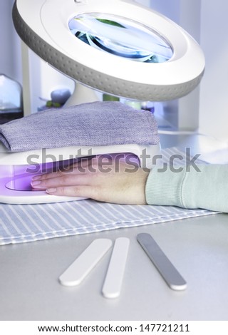 Nail salon, a female hand inside drying UV light machine. This treatment increases a risk of skin cancer