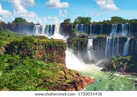 Iguazu waterfalls in Argentina, view from Devil's Mouth, close-up on powerful water streams creating mist over Iguazu river. Sub-tropical shrubs and trees in Iguasu river valley..