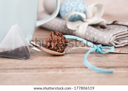 Chocolate truffle in tea spoon next to mug and loose leaf tea in pyramide