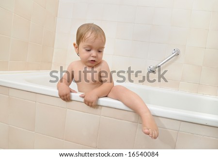 one year old baby with wet curly hair climbs out of bath tub