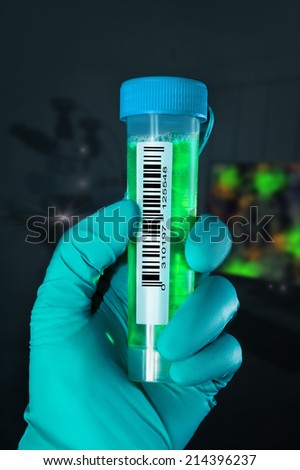 Gloved hand holds bar-coded liquid sample in microscopy room