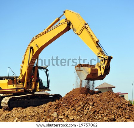 A large yellow excavator moving a large pile of dirt with debris falling from the bucket.