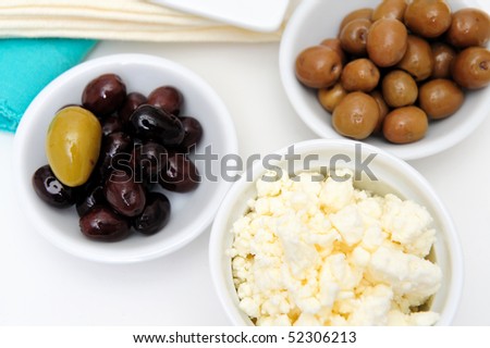Green and black marinated olives in small white bowls with blue and cream colored napkins in the background