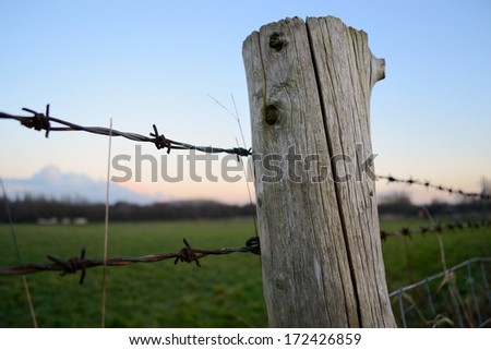 View through the barbed wire fence as the sun goes down near Standish, England.