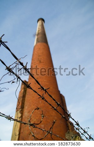 Barbed wire with old brick smokestack in background.