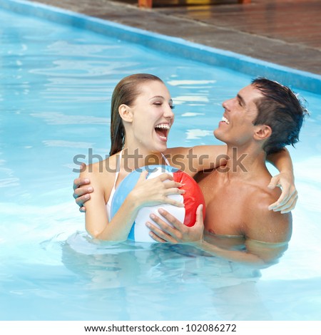Happy attractive couple having fun in pool with beach ball