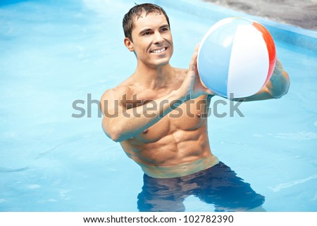 Smiling attractive man playing with water ball in swimming pool