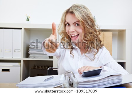 Happy business woman in office with files holding thumbs up