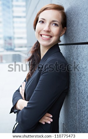 Happy confident business woman leaning on wall in the city