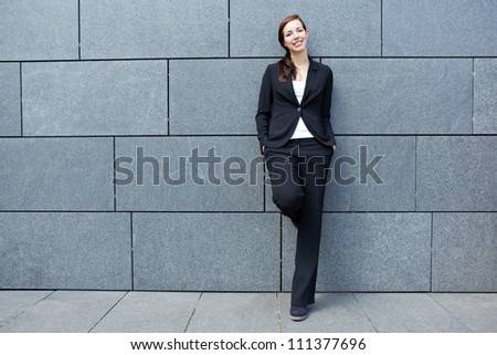 Smart happy business woman leaning on wall in the city
