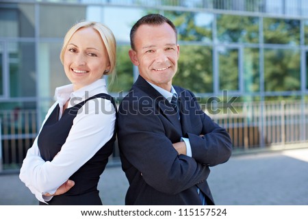 Business man and smiling woman leaning back on back outside the office