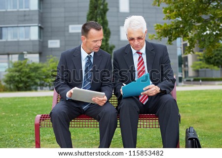 Two business people with tablet computer signing contract on a park bench
