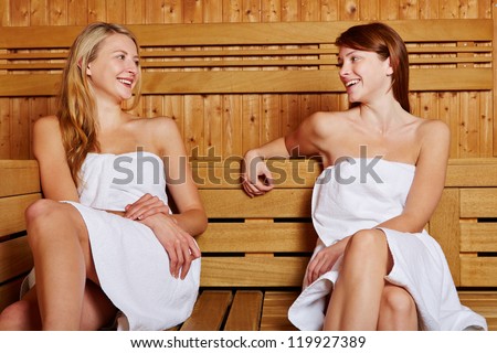 Two women sitting smiling in sauna and talking to each other