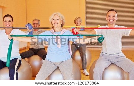 Group of happy senior people doing back training with exercise band in gym