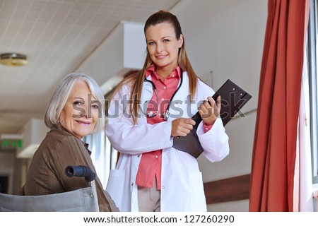 Senior woman in wheelchair in hospital with a nurse with clipboard