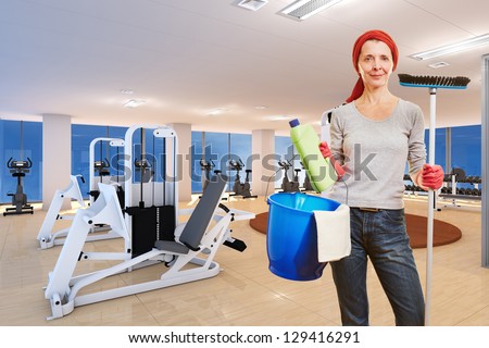 Elderly cleaning lady with cleaning supplies standing in a fitness center