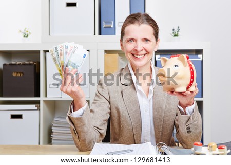 Happy elderly business woman with piggy bank and Euro money in her office
