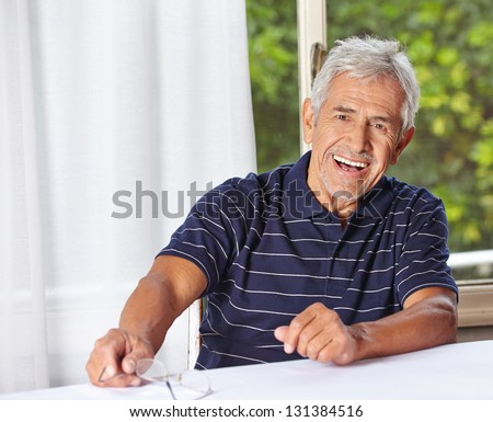 Happy smiling senior man sitting with reading glasses at a table