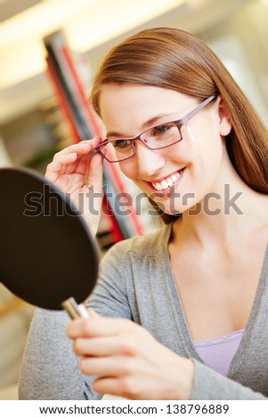Happy smiling woman with new glasses looking in mirror at optician