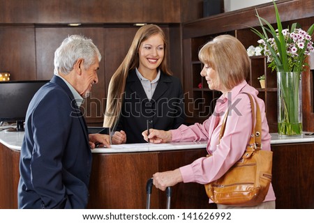 Senior couple in hotel signing form at reception