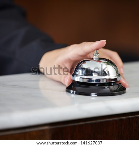 Female hand ringing hotel bell at the counter with index finger