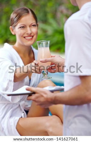 Waiter giving cocktail to attractive woman at hotel pool