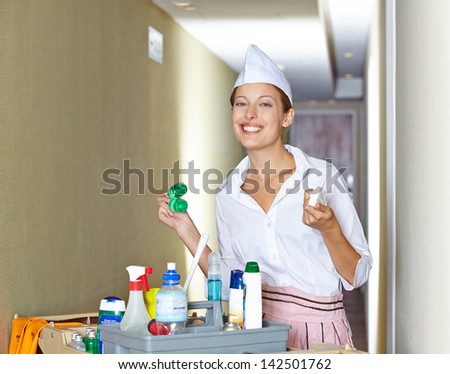 Smiling hotel maid standing with cleaning cart in corridor